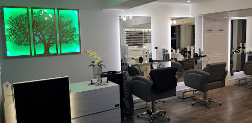 Inside Infinity Salon in St Helier: styling chairs at lit mirrors, a product display and a backlit green tree wall panel.